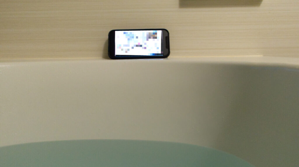 風呂釜の縁にiPhoneを設置し、テレビが流れている